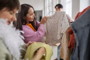 A person holds up a colorful, speckled sweater inside a bustling clothing store, surrounded by racks of clothes.