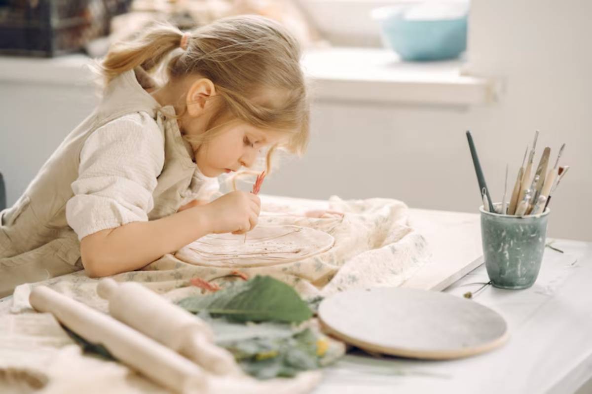 A child is focused on painting a decorative plate with tools and art supplies scattered around a bright, cozy workspace.