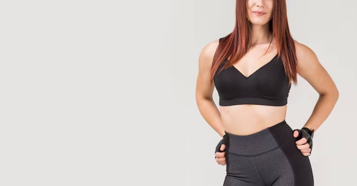 A fit woman with long, straight brown hair poses confidently in a black sports bra and gray leggings, showcasing activewear style.