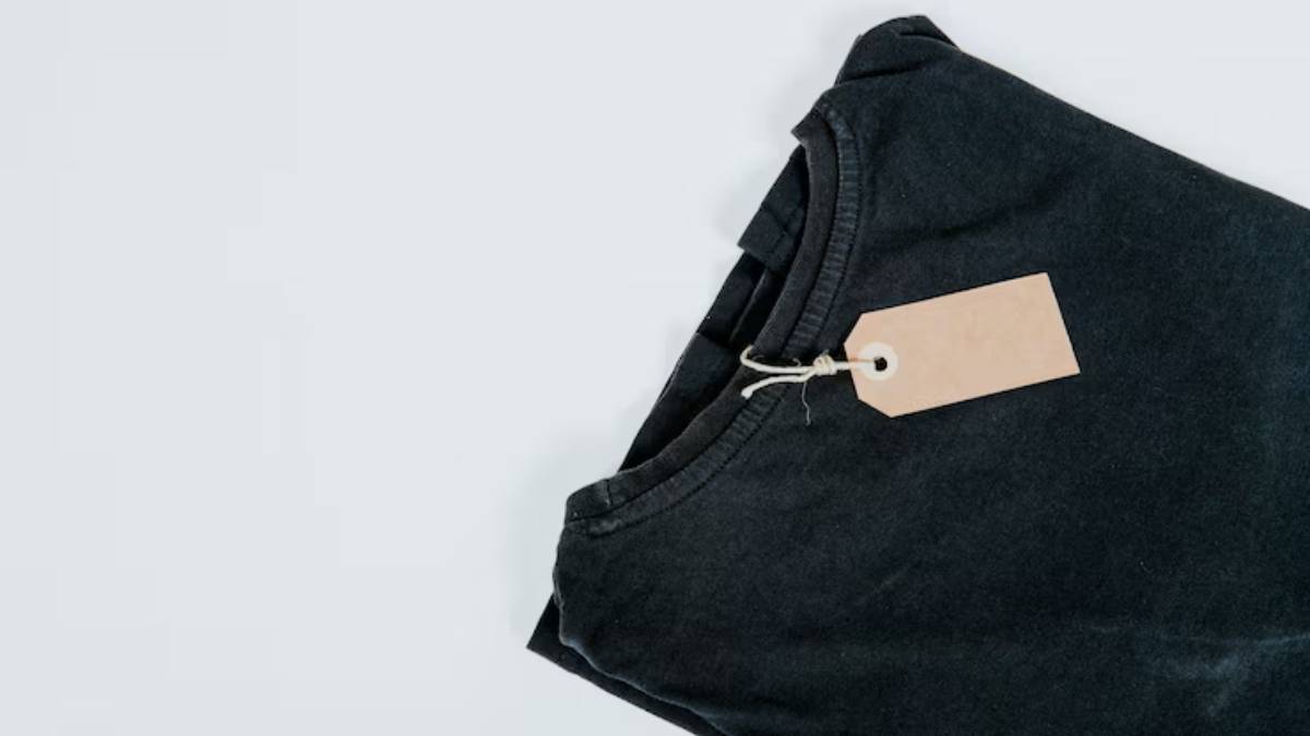 A folded black shirt with a blank brown price tag attached, resting on a light gray background.