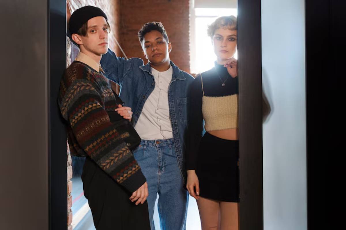 Three young adults pose together in a trendy indoor space, showcasing stylish outfits amidst a backdrop of brick walls and natural light.