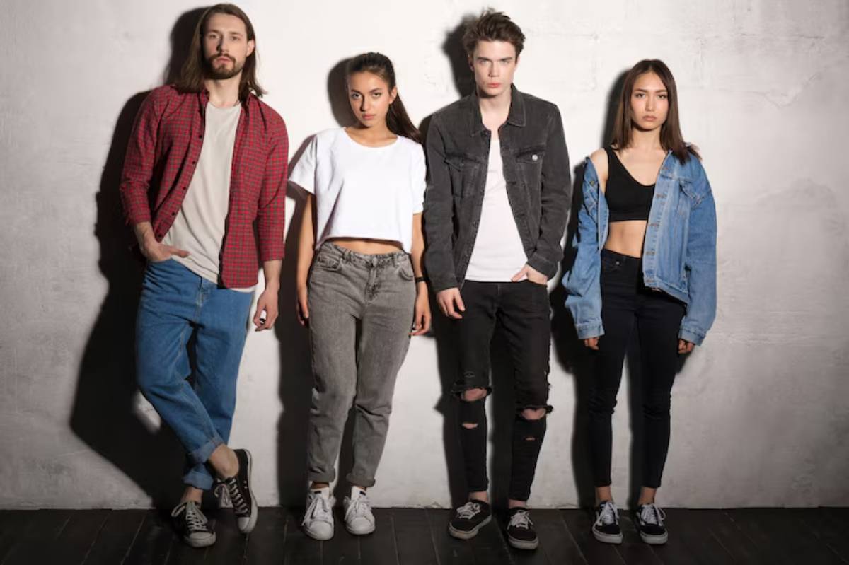 Four young adults stand confidently against a textured white wall, each dressed in stylish casual attire.
