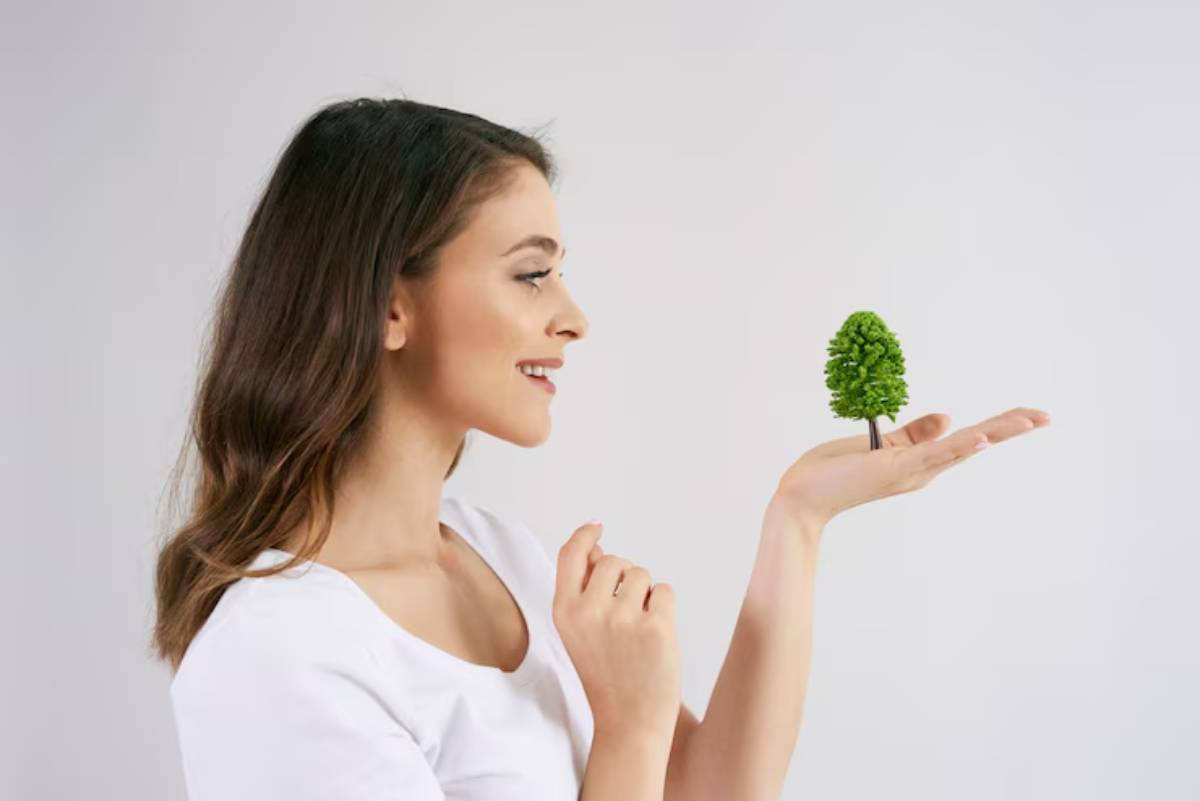 A person holds a small green tree model in their hand against a neutral background, symbolizing nature and environmental consciousness.