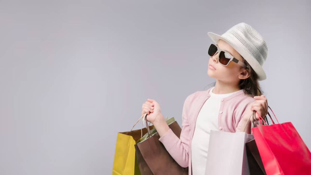 A girl in a stylish hat holds multiple shopping bags, smiling and showcasing her excitement while standing against a light gray background.