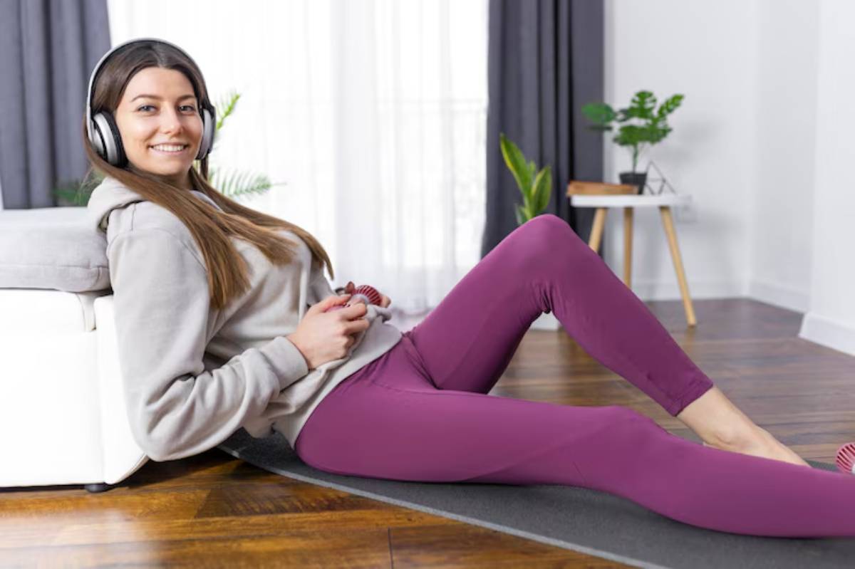 A person in headphones sits relaxed on a floor mat, gaming controller in hand, against a cozy couch in a bright living space.